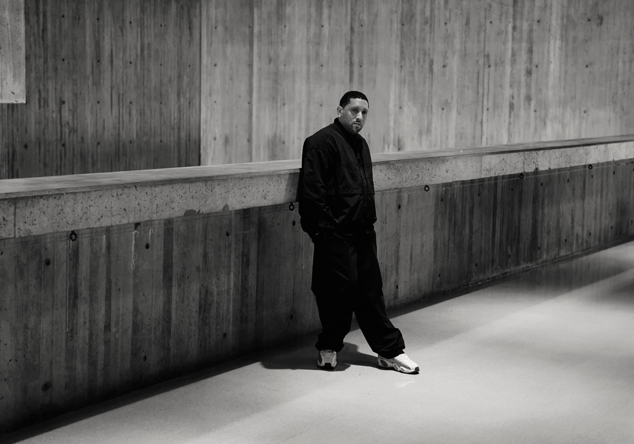 A man leans up against a wood-paneled wall.