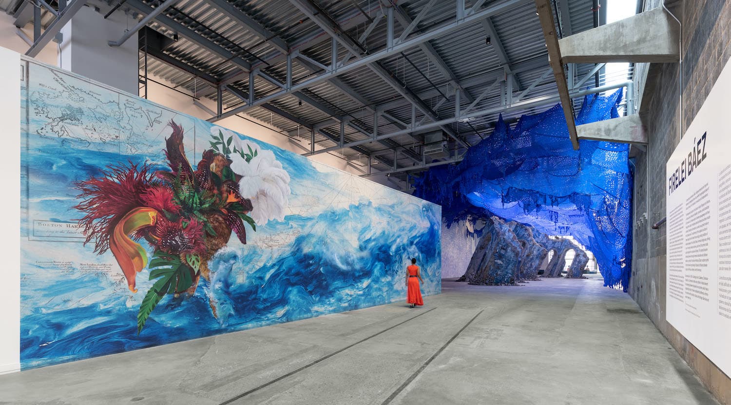 In front of a scene of blue waves by Firelei Báez, an abstract image of abundance emerges.