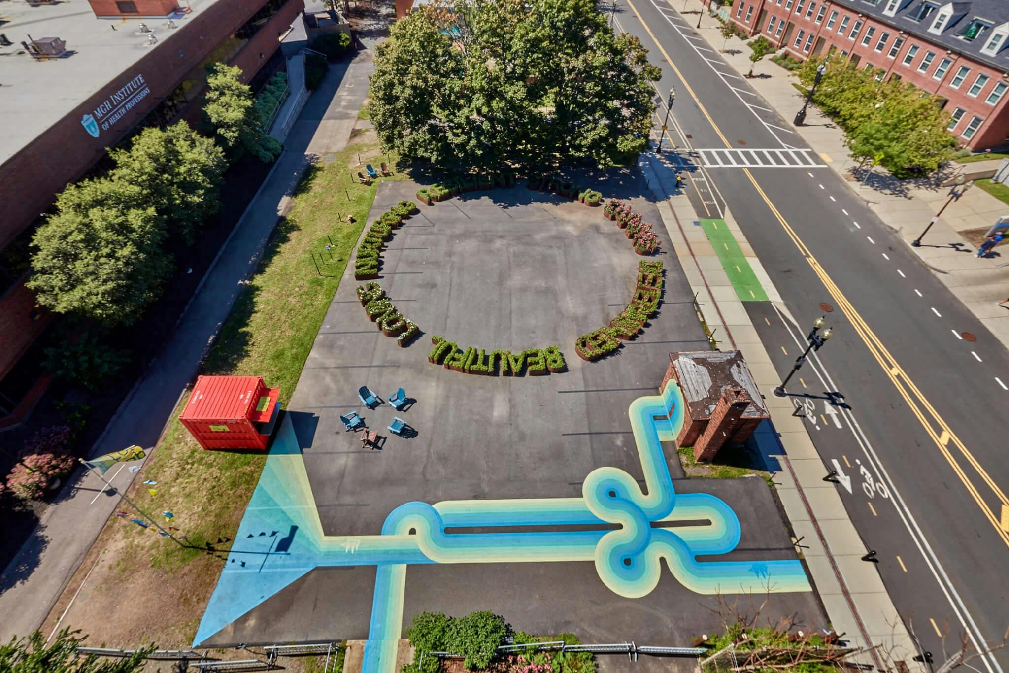 An aerial view of two vibrant public art works, featuring green letters made from plant life, in the shape of a circle.