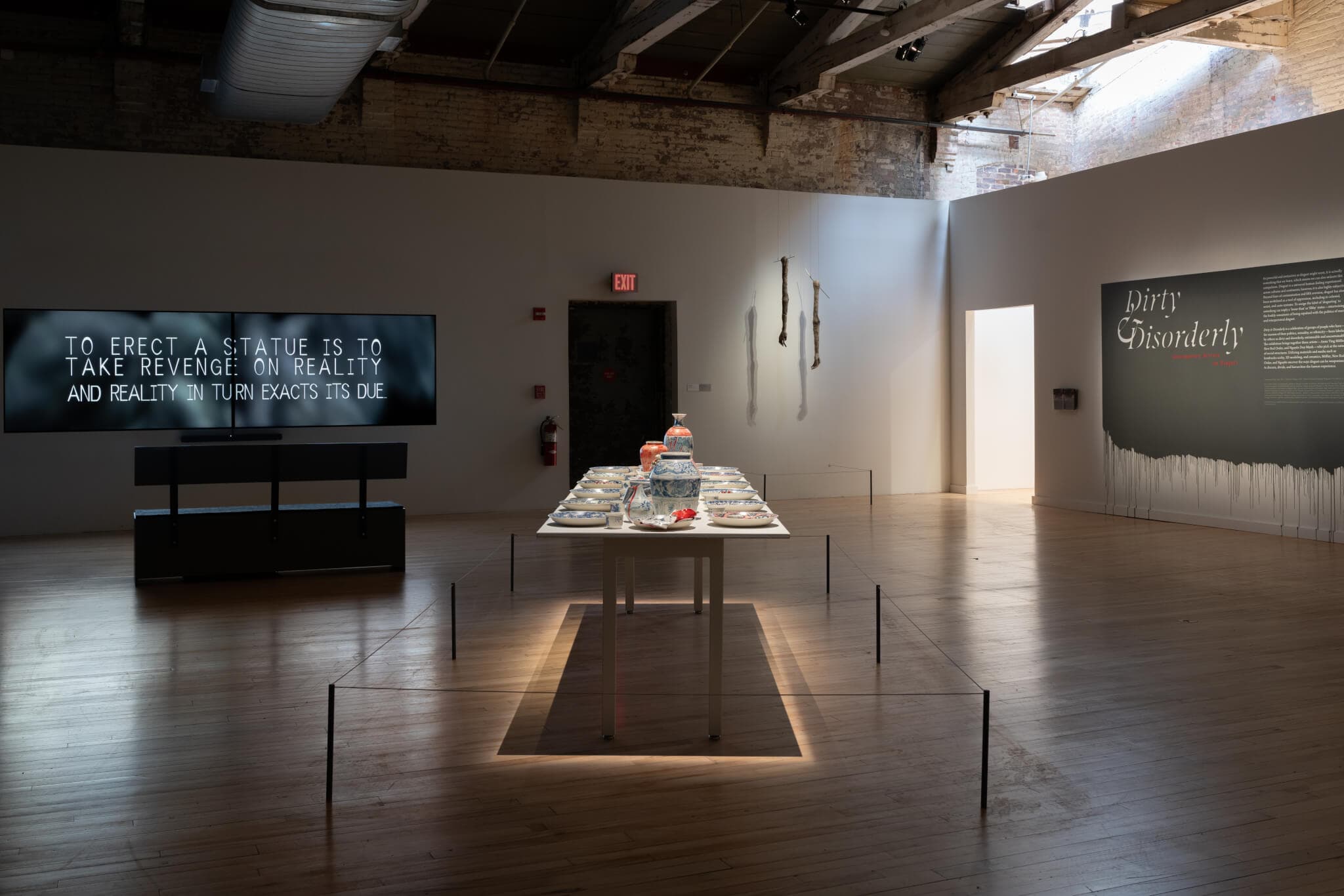 A large screen with writing and a long table with ceramic pottery.