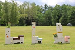 Three concrete sculptures made to look like chairs are situated in a line in a large field.