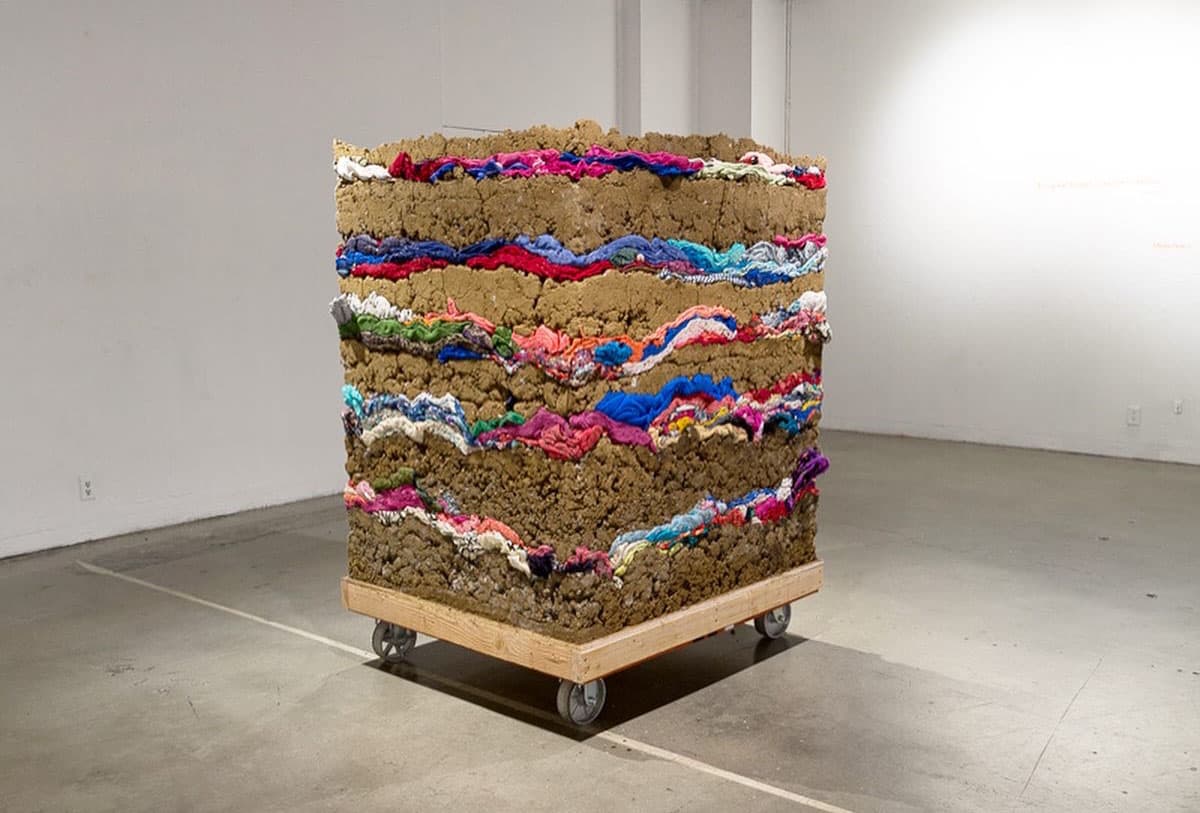 Minga Opazo's artwork made from recycled clothing, mud, and wood in a vertical formation.